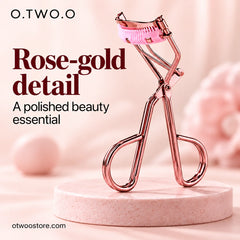 Rose-gold eyelash curler displayed upright on a soft blush pedestal