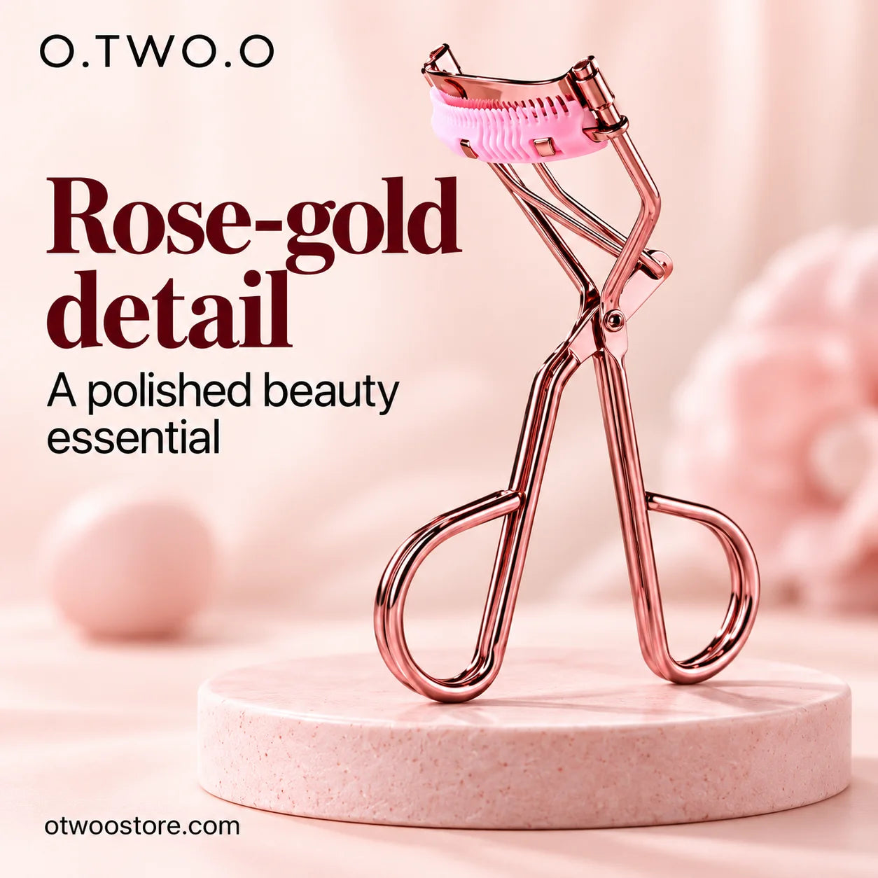 Rose-gold eyelash curler displayed upright on a soft blush pedestal